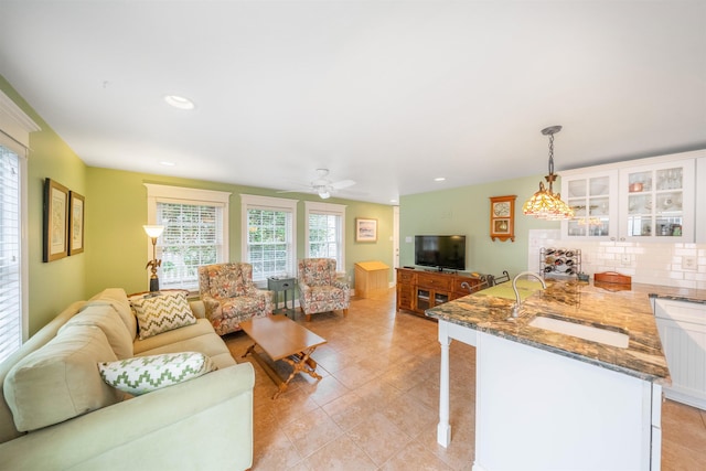 kitchen with tasteful backsplash, stone countertops, open floor plan, white cabinetry, and a sink