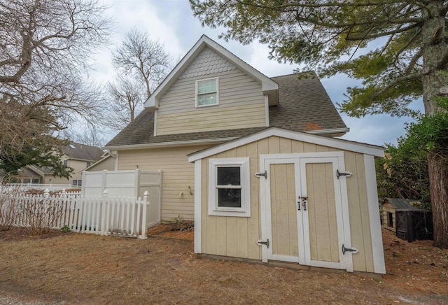 rear view of house with a shingled roof, a storage unit, fence, an outdoor structure, and board and batten siding