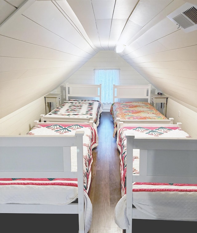 bedroom with vaulted ceiling, wood finished floors, visible vents, and wooden walls