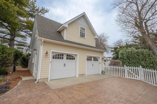 exterior space with a garage, fence, and roof with shingles