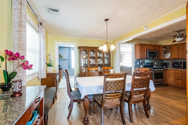 dining space with ornamental molding, light wood-style flooring, ceiling fan with notable chandelier, and visible vents