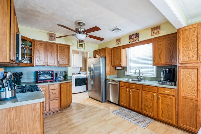 kitchen featuring light wood-style flooring, appliances with stainless steel finishes, brown cabinets, washer / clothes dryer, and a sink