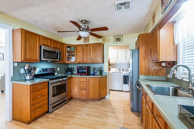 kitchen featuring appliances with stainless steel finishes, brown cabinetry, a sink, and washing machine and clothes dryer