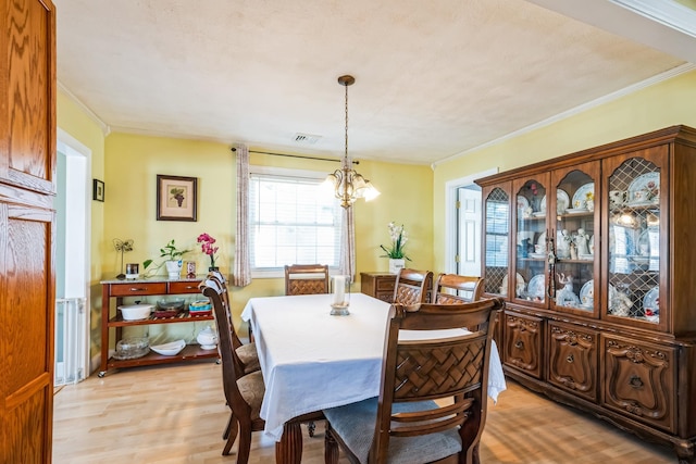 dining room featuring crown molding, a notable chandelier, visible vents, and light wood-style floors