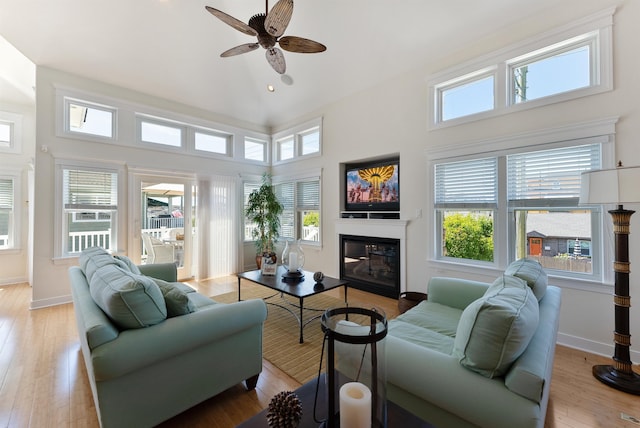 living room with ceiling fan, light wood-type flooring, and a high ceiling