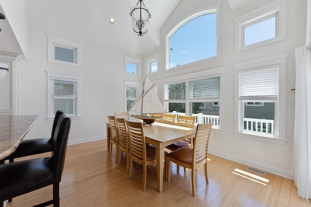 dining area with light hardwood / wood-style floors, high vaulted ceiling, and a chandelier