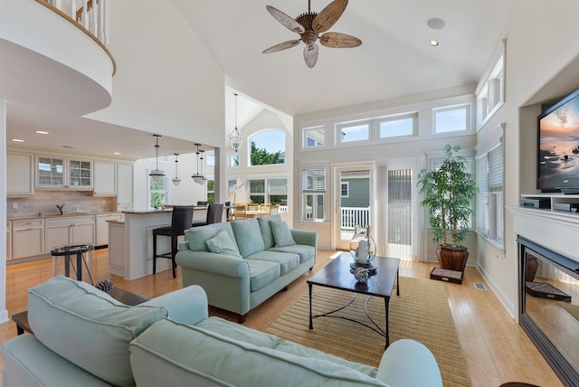 living room featuring a towering ceiling, light hardwood / wood-style floors, ceiling fan, and sink