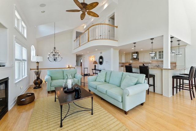 living room featuring ceiling fan with notable chandelier, a towering ceiling, and light hardwood / wood-style flooring