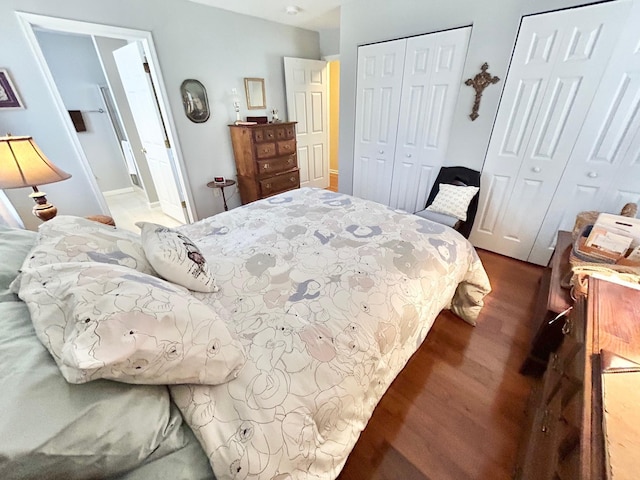 bedroom featuring dark wood-type flooring, two closets, and connected bathroom