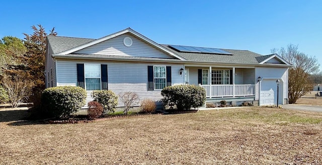 single story home featuring a porch, a front yard, roof mounted solar panels, driveway, and an attached garage