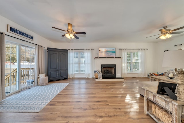 living room featuring light wood-style floors, a fireplace with raised hearth, and a ceiling fan