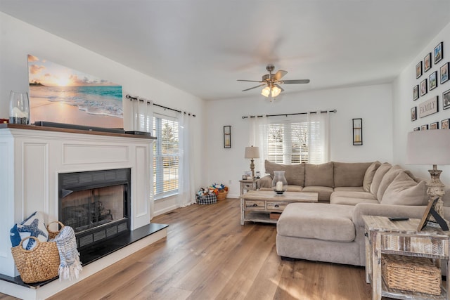 living area with light wood-style floors, baseboards, a fireplace with raised hearth, and a ceiling fan