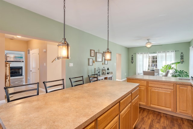 kitchen featuring dark wood-style floors, decorative light fixtures, a fireplace, light countertops, and ceiling fan