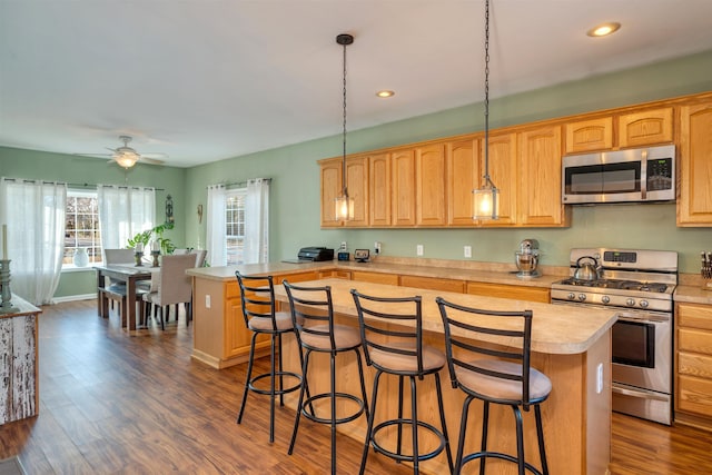 kitchen featuring stainless steel appliances, a breakfast bar, a kitchen island, light countertops, and dark wood finished floors