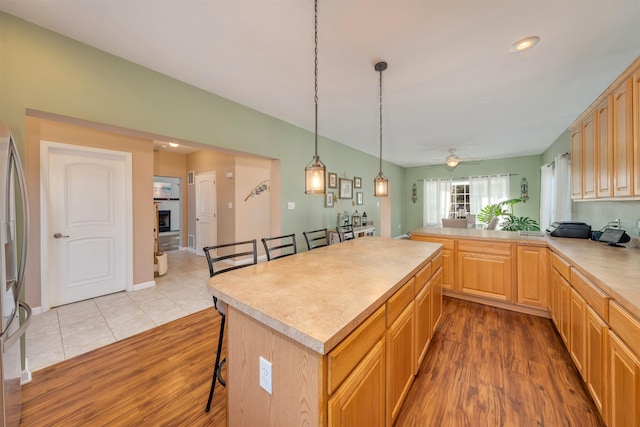 kitchen with a breakfast bar, light countertops, a fireplace with raised hearth, light brown cabinetry, and wood finished floors