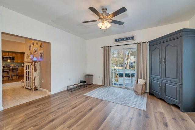 living area with a ceiling fan, light wood-style flooring, and baseboards