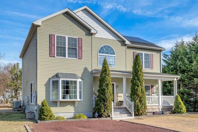 view of front of property with central AC, a porch, and roof mounted solar panels