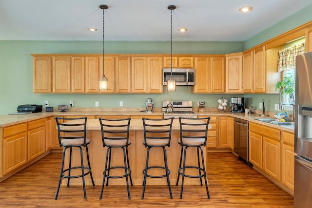 kitchen with stainless steel appliances, wood finished floors, light countertops, and a kitchen breakfast bar