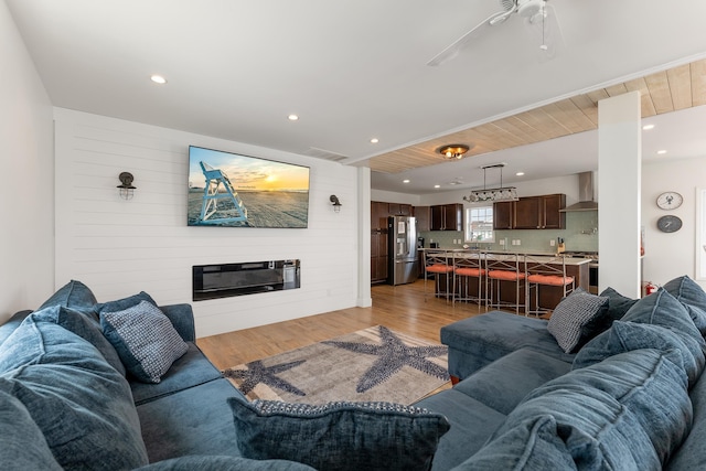 living area with light wood-style floors, recessed lighting, visible vents, and a glass covered fireplace