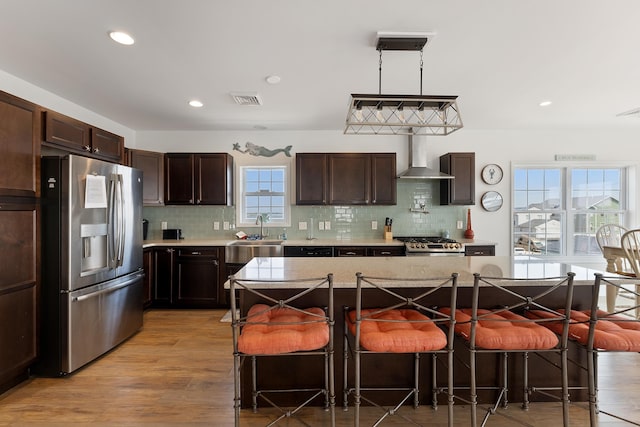 kitchen featuring visible vents, stove, a sink, wall chimney range hood, and stainless steel fridge