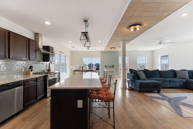 kitchen featuring wall chimney range hood, a kitchen bar, stainless steel appliances, and wood finished floors