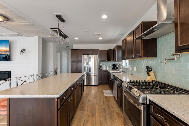 kitchen with stainless steel appliances, wood finished floors, visible vents, wall chimney range hood, and a center island