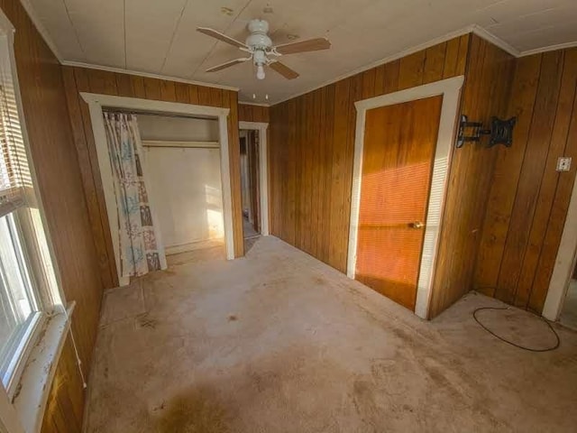 unfurnished bedroom with a closet, wood walls, crown molding, and a ceiling fan