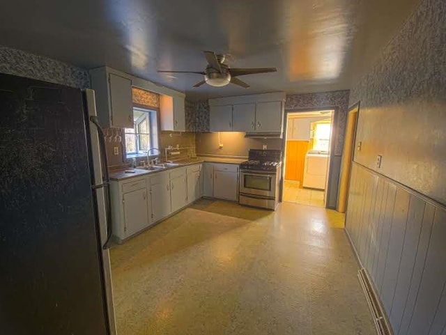 kitchen featuring ceiling fan, wainscoting, washer / clothes dryer, stainless steel appliances, and a sink