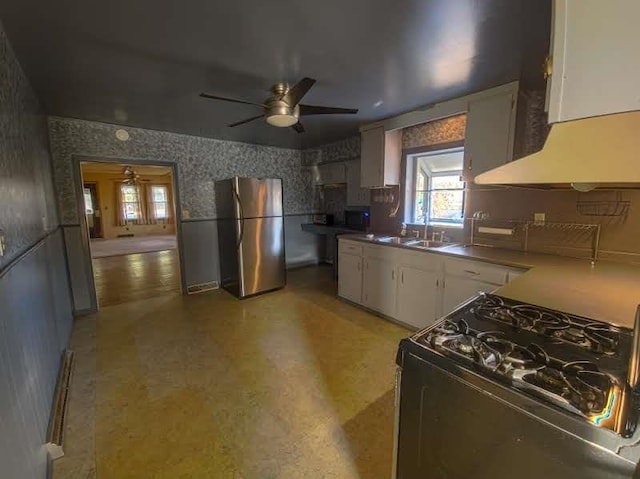 kitchen with a sink, white cabinetry, freestanding refrigerator, black gas range oven, and wallpapered walls