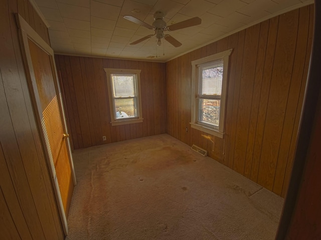 empty room with visible vents, ornamental molding, wooden walls, carpet flooring, and ceiling fan