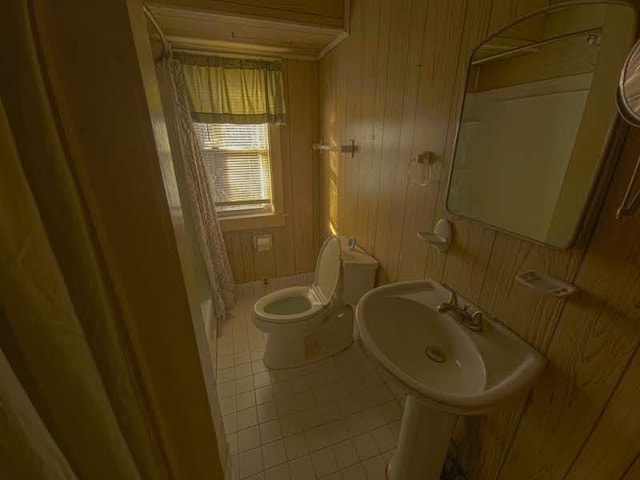 bathroom featuring a shower with curtain, toilet, a sink, wooden walls, and tile patterned flooring