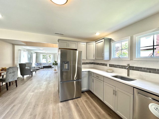 kitchen with sink, a healthy amount of sunlight, gray cabinets, appliances with stainless steel finishes, and light wood-type flooring