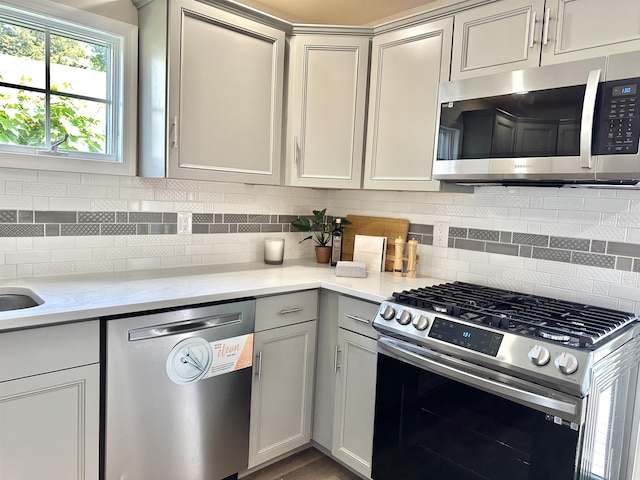 kitchen featuring decorative backsplash, gray cabinets, light stone countertops, and appliances with stainless steel finishes