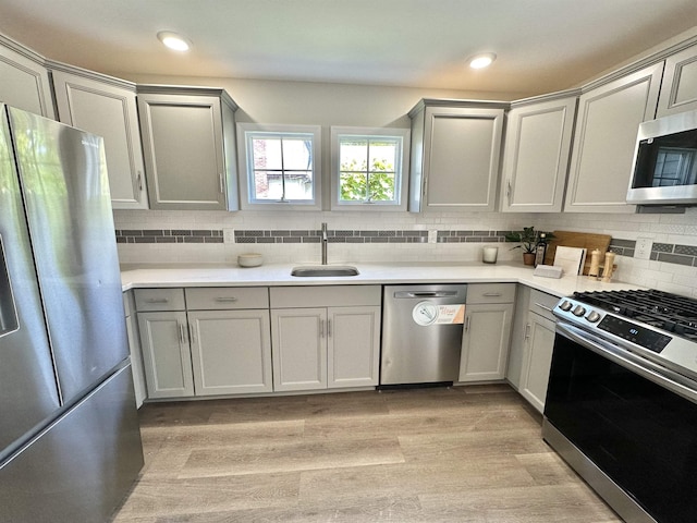 kitchen featuring sink, light hardwood / wood-style flooring, gray cabinets, appliances with stainless steel finishes, and tasteful backsplash