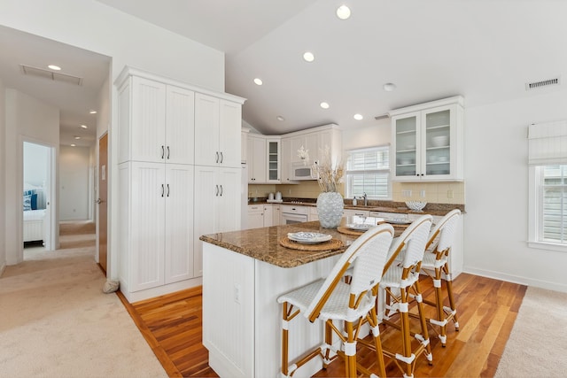 kitchen featuring a center island, white cabinetry, dark stone counters, a breakfast bar, and light colored carpet