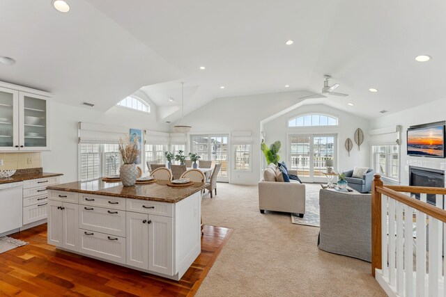 kitchen with white cabinets, dark stone counters, vaulted ceiling, ceiling fan, and light colored carpet