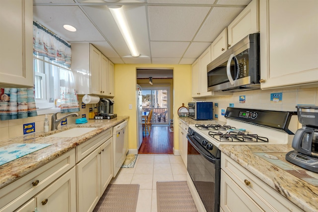 kitchen featuring sink, light tile patterned floors, a paneled ceiling, white dishwasher, and gas range