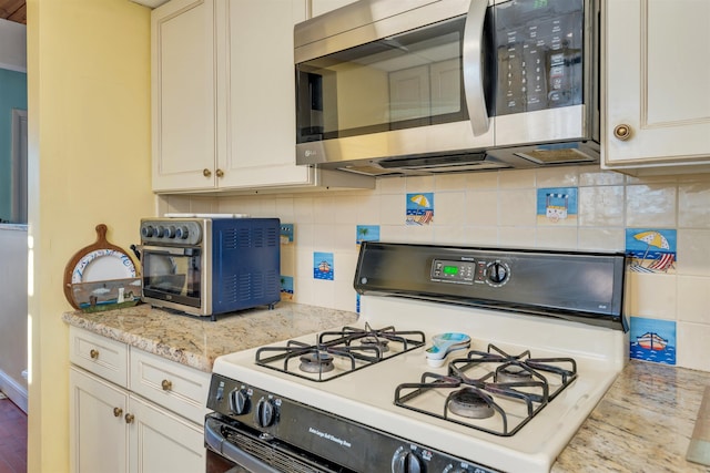 kitchen with white range with gas cooktop, white cabinetry, tasteful backsplash, and light stone countertops