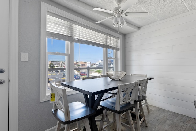 dining area with ceiling fan, wood finished floors, wooden walls, and a textured ceiling