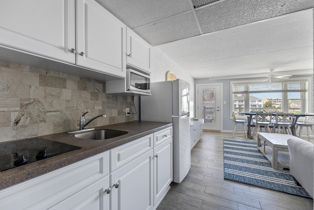 kitchen with stainless steel microwave, a sink, dark countertops, white cabinetry, and decorative backsplash