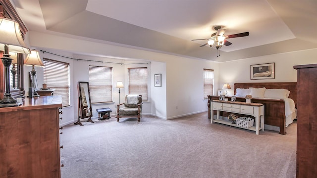 bedroom featuring ceiling fan, multiple windows, a tray ceiling, and light carpet