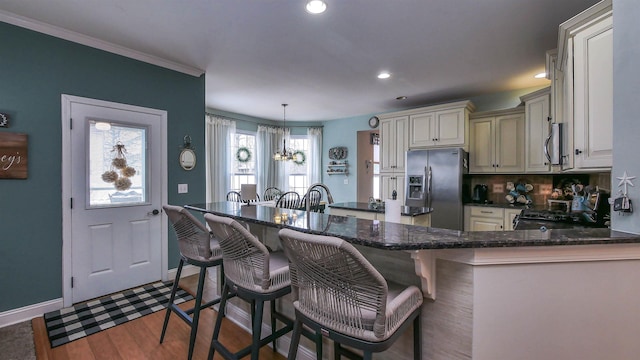 kitchen featuring decorative light fixtures, wood-type flooring, a kitchen bar, stainless steel appliances, and cream cabinetry