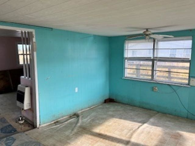 empty room with heating unit, a wealth of natural light, and ceiling fan