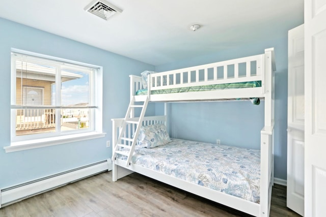 bedroom featuring visible vents, wood finished floors, and a baseboard heating unit