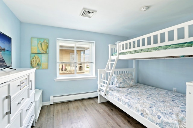 bedroom with a baseboard heating unit, visible vents, wood finished floors, and baseboards