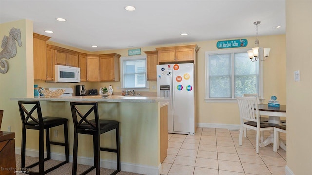 kitchen featuring kitchen peninsula, a healthy amount of sunlight, white appliances, and a notable chandelier