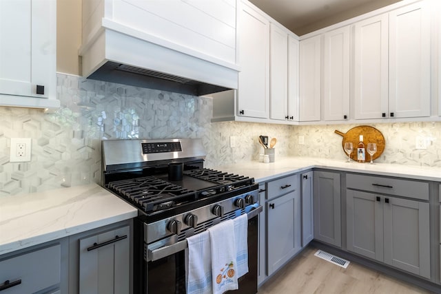 kitchen featuring white cabinetry, light stone countertops, stainless steel gas range oven, premium range hood, and backsplash