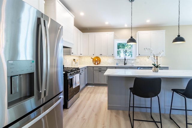 kitchen featuring light stone countertops, gray cabinetry, stainless steel appliances, white cabinetry, and hanging light fixtures