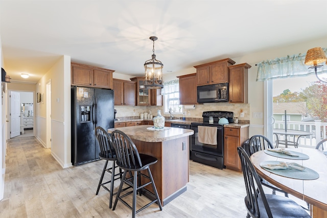 kitchen featuring tasteful backsplash, black appliances, decorative light fixtures, a center island, and light hardwood / wood-style floors