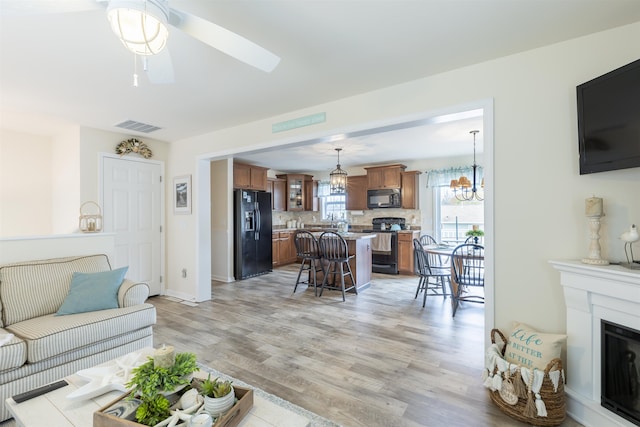 living room featuring a stone fireplace, ceiling fan with notable chandelier, and light wood-type flooring